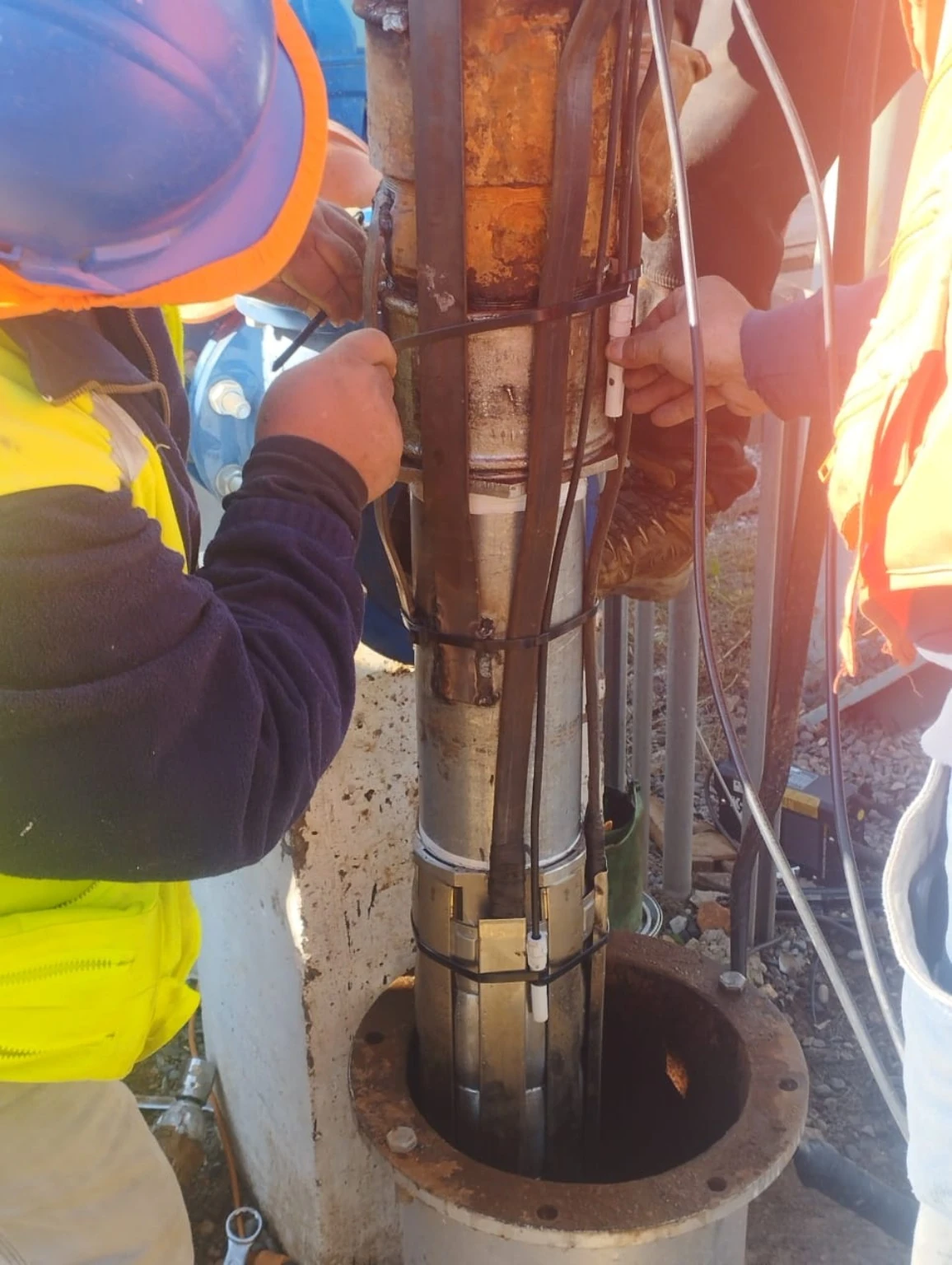 Trabajadores interviniendo el conjunto de una bomba sumergible sobre la boca de un pozo de agua potable rural.